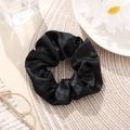 Classic black satin scrunchie with soft pleats on a minimalist woven mat background - Black