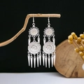 Detail shot of ethnic silver earrings with cone tassels hanging on a rustic wooden branch - Sunflower Mandala Spiked Tassel Style (E3831)