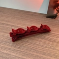 Close-up of red velvet hair clip with three decorative flowers on a wooden surface - Red