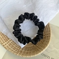 Elegant black satin scrunchie with pleated silk texture on a natural woven basket - Black