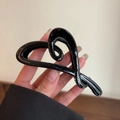 Gros plan d'une pince à cheveux noire brillante en forme de cœur tenue à la main - Pince à Cheveux Cœur Noir Brillant
