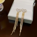 Elegante goldene Quastenohrringe mit Herz-Strass-Anhänger an einer Schmuckschatulle hängend - Silbernadel / Gold