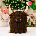 Peluche vache Highland marron avec couronne de fleurs roses dans un décor naturel - Vache des Highlands Brune
