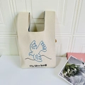 Detailed close-up of beige knitted tote bag with blue bird pattern and fly like bird text - Swallow Beige
