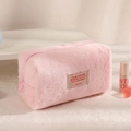 Detailed close-up of pink plush makeup bag featuring embroidered text and zipper closure - Pink