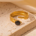 Detail eines goldenen Federrings mit schwarzem Stein auf elegantem Steinhintergrund - Schwarzer Stein Feder Stil (TYR0772)