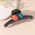 Dettaglio di una pinza per capelli nera con grandi ornamenti a sfera arancioni e blu-verdi - Caffè Blu
