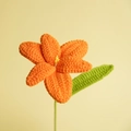 Handmade crochet orange lily flower with green stem and leaf against a yellow background - Orange