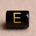 Macro shot of black cylindrical bead with gold stamped letter E for DIY jewelry - Letter E