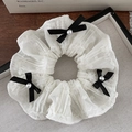 Detalle de scrunchie de encaje blanco con lazos negros y perlas sobre tela de rejilla - Blanco