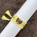 Macro detail of hand-woven yellow bracelet with purple crystal bear head and tassels - Yellow