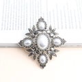 Spilla vintage in lega con perle bianche e strass grigi su un libro elegante - grigio scuro
