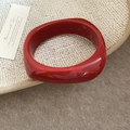 Close-up of a thick red resin square bangle with white swirl texture on a beige background - Bright Red with White Veins
