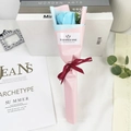 Detailed view of a single blue soap rose bouquet in pink wrap with a red ribbon - Ice Blue Rose