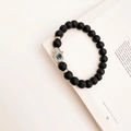Detail of black lava stone beads and silver Hamsa Hand charm with blue evil eye on a book - Black Lava Stone