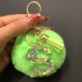 Detail of green faux fur pompom keychain with transparent resin letter S and gold tassel - Letter S