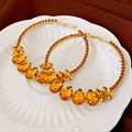 Detailed shot of gold hoop earrings with amber pear-cut stones on a white relief plate - Champagne Rhinestone (Silver Pin)