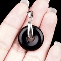 Polished black gemstone donut pendant with silver metal clasp held by hand - 20mm Obsidian