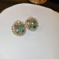 Macro-opname van gouden oorbellen met groene edelstenen en turquoise kralen op een schaal - Gouden Luxe Smaragd Ovaal Stijl (21#)