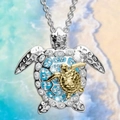 Close-up of double turtle necklace with blue crystals and gold accents on a beach backdrop - Gold Necklace
