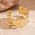 Detailaufnahme goldener Armreif mit unregelmäßiger Hammerschlagstruktur auf Stein - Gold