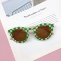Detail of green and beige checkered kids sunglasses with UV400 lens on a magazine - Green Plaid