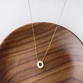 Collier minimaliste en or avec pendentif rond en nacre sur texture bois sombre - Lettre O