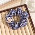 Blue and white plaid scrunchie with red floral pattern and heart tag on beige display - Label Blue Stripe