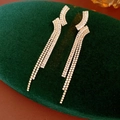 Macro shot of gold geometric tassel earrings with zircon pave on green velvet base - Gold