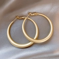 Detail shot of matte gold crescent hoop earrings on elegant silver silk fabric - Matte Thick Hoop / Matte Gold