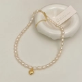 Dettaglio di collana con perle barocche e ciondolo a cuore dorato su vassoio bianco - Ciondolo a cuore
