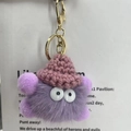 Detail of a purple fluffy monster keychain with pink knit hat and golden clasp hardware - Light Purple