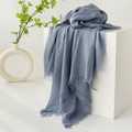 Blue-grey cotton linen scarf with fringe edges displayed on a minimal white cube pedestal - Haze Blue
