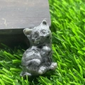 Close-up of 1.2 inch hand-carved natural stone cat figurine on a green lawn - Larvikite