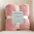 Pink embossed leaf flannel blanket folded with ribbon on a beige sofa - Pink