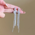 Détail de boucles d'oreilles pendantes argentées avec strass brillants tenues à la main - Argenté