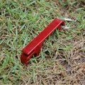 Compact red aluminum alloy beer bottle opener keychain shown outdoors on green grass - Red
