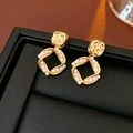 Macro shot of gold square earrings with white pearls on a black leather display - Gold