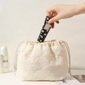 Detail view of white quilted drawstring bag being filled with hand cream and cosmetics - White Shell