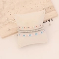 Close-up of Bohemian layered bracelets with colorful beads on a cream jewelry pillow - White