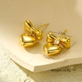 Detalle macro de pendientes dorados de lazo y corazón con cristales sobre piedra - Pendientes de Botón con Colgante de Corazón y Lazo