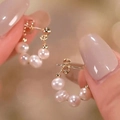 Macro shot of elegant round pearl earrings in a gold circular layout held by a hand - Gold Hoop Pearl Earrings