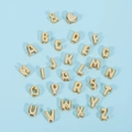 Detailansicht goldener 18K Buchstabenperlen und Herzanhänger auf blauem Grund - Nummer 3 / Gold