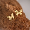 Close-up of polished gold butterfly stud earrings on textured reddish-brown rock - Gold Butterfly (EH127)