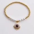 Dettaglio macro del bracciale a sfere dorate con perle e ciondolo occhio rosso - Rosso Scuro