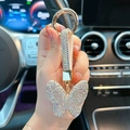 Funkelnder Schmetterling-Schlüsselanhänger mit Strass und Goldring im Autoinnenraum - AB Weiß