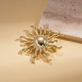 Macro view of a polished gold sunburst brooch with wavy rays on a stone surface - Gold