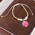 Dettaglio di un braccialetto di perline fatto a mano con ciondolo rosa su fondo legno - Rosa