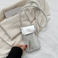 Schicke silberne Mini-Handytasche mit Schultergurt auf beigem Blazer und Kunstbuch - Silber