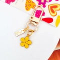Yellow enamel flower keychain with gold clasp and a handmade metal tag on white base - Yellow